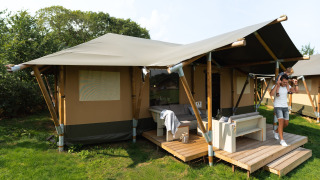 Familie vor einem luxuriösen Safarizelt namens Safaritent Medley mit Terrasse und Möbeln in der Natur.