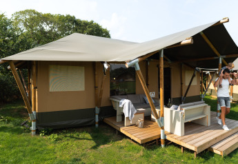 Famiglia davanti a una tenda safari di lusso, Safaritent Medley, con veranda e arredi moderni immersi nel verde.