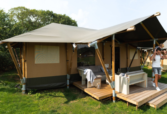 Familie vor einem luxuriösen Safarizelt namens Safaritent Medley mit Terrasse und Möbeln in der Natur.