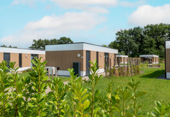 Moderne Water lodge 2 met hot tub bij Hofparken Wiltershaar in Nederland, omringd door gras en bomen.