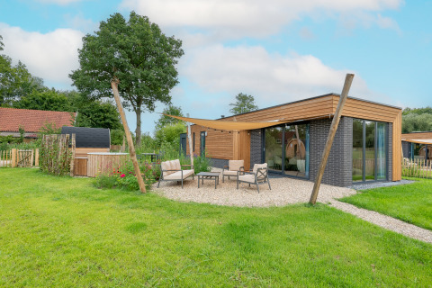 Lodge moderne à façade bois, grandes baies vitrées et coin salon extérieur confortable sur pelouse.