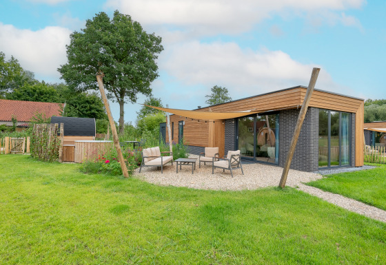 Lodge moderne à façade bois, grandes baies vitrées et coin salon extérieur confortable sur pelouse.
