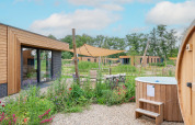 Moderne Lodge mit Holzverkleidung, Außenwhirlpool, Blumenbeet und Sonnenschutz bei klarem Himmel.