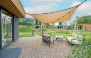 Gemütlicher Außenbereich einer modernen Lodge mit Markise, Sitzgruppe und Blick auf grüne Umgebung.