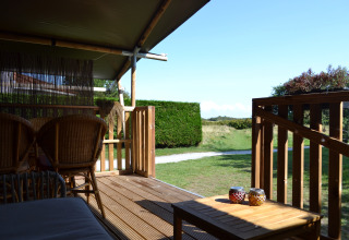 Houten veranda met rotanstoelen en groen uitzicht bij een safaritent op Parc Koudenburg, Nederland.