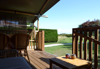 Terrazza in legno con mobili in vimini e vista verde presso una tenda safari al Parc Koudenburg, Paesi Bassi.