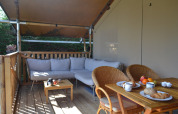 Überdachte Terrasse mit Sofa, Esstisch und Frühstück im Safarizelt bei Parc Koudenburg, Niederlande.