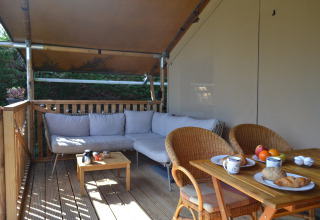 Terrazza all’aperto con divano, tavolo da pranzo e colazione in tenda safari al Parc Koudenburg, Paesi Bassi.
