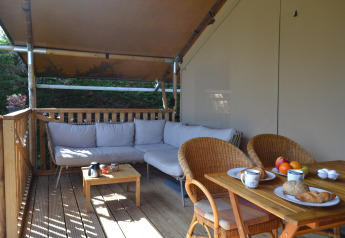 Terrazza all’aperto con divano, tavolo da pranzo e colazione in tenda safari al Parc Koudenburg, Paesi Bassi.