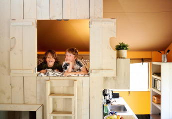 Two kids relaxing in a treehouse, Safari Boomhut with sanitary facilities at Camping Goorzicht in the Netherlands.