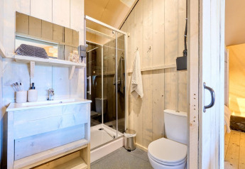 Bagno luminoso in una sistemazione glamping con pareti di legno, doccia, lavandino e toilette.