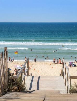 A sunny beach with swimmers and wooden walkway, photographed near Aureilhan in Nouvelle-Aquitaine, France.