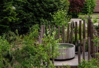 Een houten hot tub omringd door palen in een groene tuin bij Sandberghe vakantiepark, Noord-Brabant.