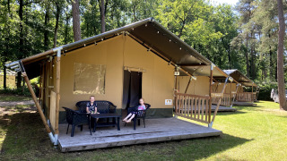 Due bambini siedono sulla veranda di una tenda safari nel bosco, con altre tende simili sullo sfondo.