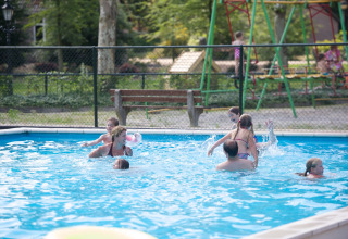 Kinderen en volwassenen genieten van zwemmen in een buitenzwembad bij vakantiepark Sandberghe.