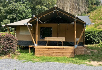 Safaritent met privé sanitair, houten terras en bank, omgeven door groen en natuur.