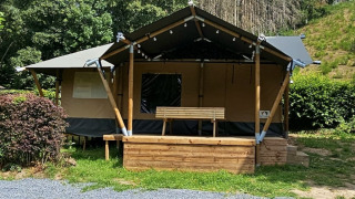 Safari tent with private sanitary facilities, wooden porch and bench, surrounded by lush greenery.