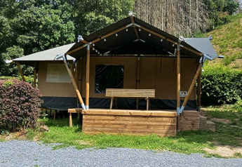 Safari tent with private sanitary facilities, wooden porch and bench, surrounded by lush greenery.