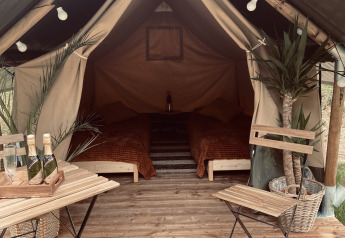 Tente safari Duo accueillante avec plancher en bois, deux lits, plantes, table, chaises et champagne.
