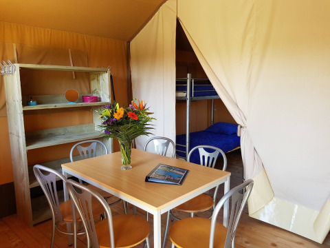 Interior of a safari tent with dining table, chairs, bunk bed, and flowers at a Dutch holiday park.