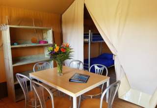 Interieur van een safaritent met tafel, stoelen, stapelbed en bloemen in een recreatiepark in Nederland.
