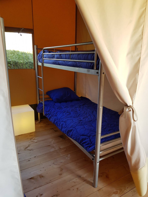 Vista interna di tenda safari con letto a castello, biancheria blu e pavimento in legno al Recreatiepark de Scherpenhof.