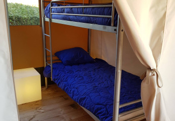 Vista interna di tenda safari con letto a castello, biancheria blu e pavimento in legno al Recreatiepark de Scherpenhof.