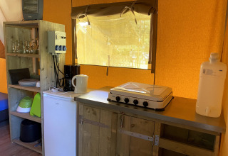 Küchenbereich eines Safarizelts im Vakantiepark Bonte Vlucht, mit Herd, Kühlschrank und Geschirr.