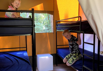 To børn hygger sig på køjesenge i en Safaritent på Vakantiepark Bonte Vlucht, Holland, med sollys.