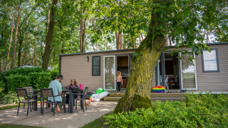 Familie nyder en afslappet dag udenfor ved et Extra Luxe Stacaravan mobilhome omgivet af træer.