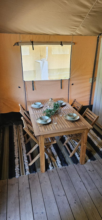 Essbereich mit Holztisch und Stühlen in einem Safari-Zelt mit Fenster bei Camping Reiler in Luxemburg.