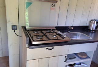 Compact kitchenette with gas stove, sink, and kettle inside safari tent at Camping Reiler, Luxembourg.