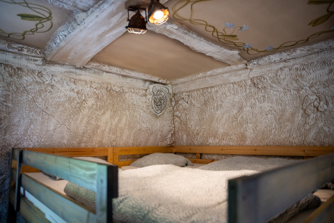Etagenbett im Hobbit-Haus im Familiepark Goolderheide, Belgien, mit rustikaler Wand und verziertem Deckenmotiv.