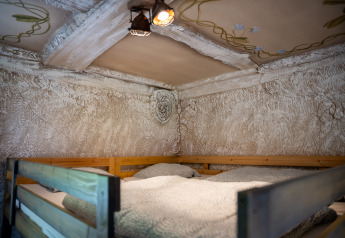 Litera acogedora en la Hobbit huisje del Familiepark Goolderheide, Bélgica, con paredes rústicas y techo decorado.