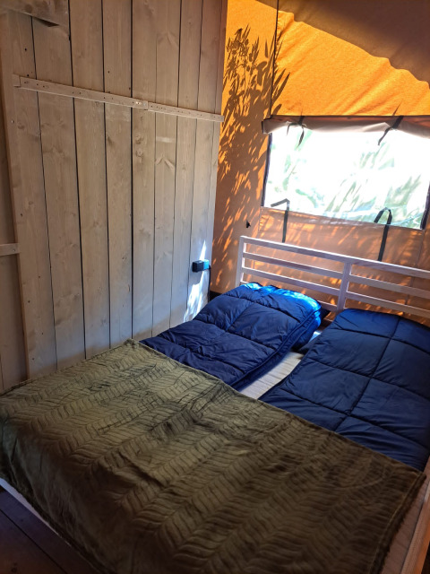 Indvendig af en safariteltseng med blåt sengetøj og grøn plaid på Camping Reiler i Luxembourg.