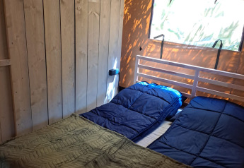 Interior of a safari tent bedroom with two sleeping bags and a green blanket at Camping Reiler, Luxembourg.