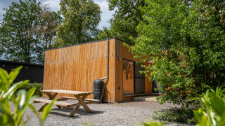 Außenansicht der Chalet-Lodge aus Holz mit Picknicktisch und grüner Bepflanzung im Sommer.