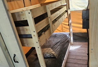 Indvendigt billede af en safaritelt med køjeseng, trægulv og varme farver på Camping Reiler i Luxembourg.