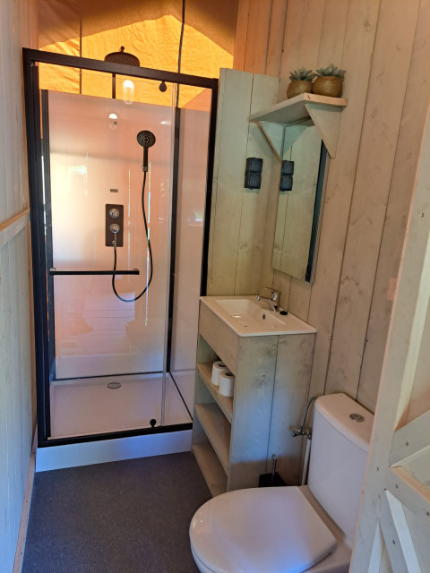 Moderne badeværelse med bruser, håndvask og toilet i en safariteltsuite på Camping Reiler i Luxembourg.