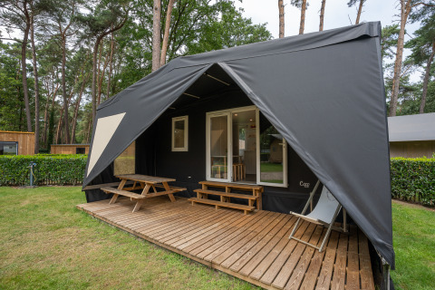 Vue extérieure d'une tente safari Cooc Tent Deluxe avec terrasse en bois, table de pique-nique et transat.