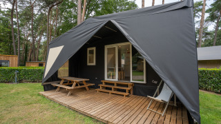Vista exterior de una tienda safari de lujo Cooc Tent Deluxe con terraza de madera y muebles al aire libre.