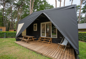 Außenaufnahme eines luxuriösen Cooc Safari-Zelt Deluxe mit Holzterrasse und Sitzmöbeln im Grünen.