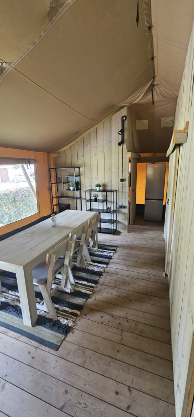 Safari-Zelt mit Holzboden, Esstisch, Stühlen und Regal bei Camping Reiler in Luxemburg.