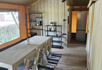 Interno di tenda safari con tavolo, sedie e pavimento in legno al Camping Reiler in Lussemburgo.