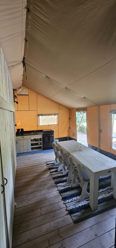 Intérieur d'une tente safari avec table à manger, chaises et cuisine au Camping Reiler au Luxembourg.