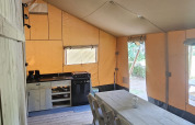Intérieur d'une tente safari avec table à manger, chaises et cuisine au Camping Reiler au Luxembourg.