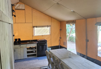 Interno di una tenda safari con tavolo da pranzo, sedie e cucina al Camping Reiler in Lussemburgo.