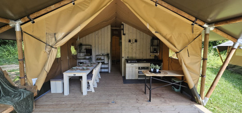 Indvendig udsigt af en safaritelt med spisebord, køkken og træramme på Camping Reiler i Luxembourg.