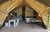 Indvendig udsigt af en safaritelt med spisebord, køkken og træramme på Camping Reiler i Luxembourg.