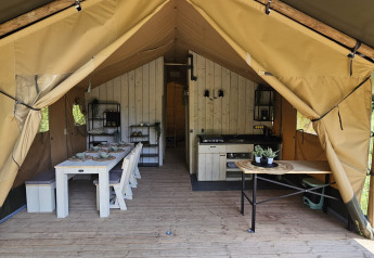 Binnenzicht van een safaritent met eettafel, keuken en houten frame op Camping Reiler in Luxemburg.